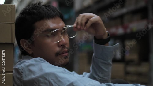 Asian Male Warehouse Worker Looking Sideways with Serious Expression. Candid Portrait in Storage FacilityAsian Male Warehouse Worker Looking Sideways with Serious Expression.