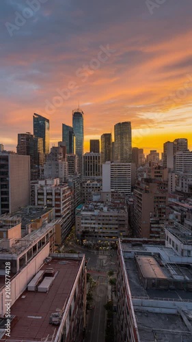 Cinematic aerial time lapse of a sprawling urban cityscape at sunset, with dynamic golden light illuminating towering skyscrapers and densely packed buildings