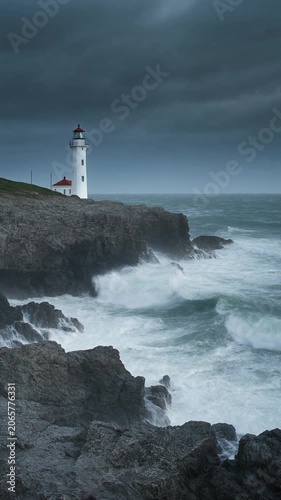 Cinematic shot of a solitary lighthouse standing stoically on a rugged, Rocky cliff face with powerful, dramatic ocean waves crashing below, under a stormy, dramatic sky