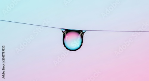 Water droplet hanging on a delicate thread against gradient sky