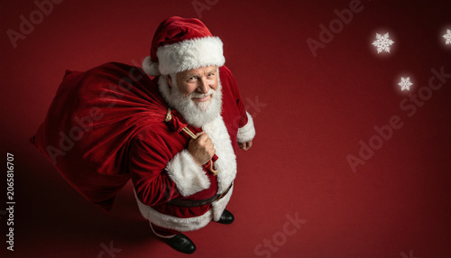 Fotografie Santa claus carrying a large red sack of gifts over his shoulder, looking up at