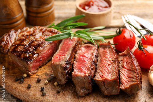 Tableau sur toile Pieces of beef steak with sauce, spices, tomatoes and rosemary served on wooden
