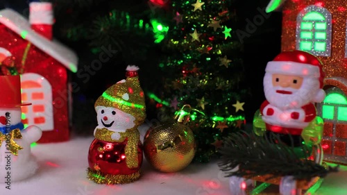 Near the houses there are two snowmen with a yellow ball and Santa Claus on a sleigh