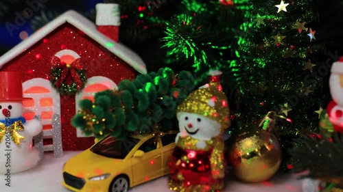 In front of the houses there are snowmen with a yellow ball and a yellow car with Santa Claus on a sleigh