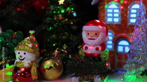 A close-up of a snowman with a yellow ball and Santa Claus on a sleigh with a yellow car in front of the houses