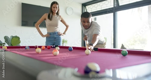 Couple playing pool at home, African American man lining up and striking cue ball taking turn