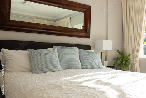 Bed with textured white duvet is anchoring room, blue-gray pillows are resting near lamp and window