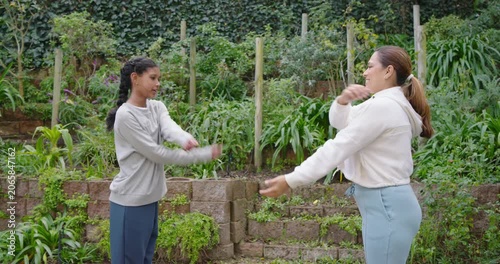 African American mom guiding teen daughter in garden, lifting hand by face, daughter mirroring keys