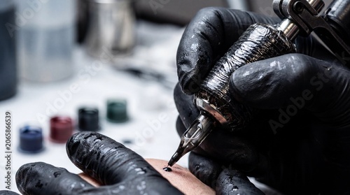Close-up of tattoo artists gloved hands using a machine to ink a design on skin
