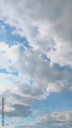 Sunny summer sky background with fluffy white clouds and bright sun rays, vertical footage 