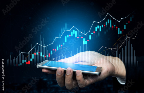 Bild auf Leinwand A close-up image of a hand holding a smartphone displaying stock market data, illustrating the intersection of technology and finance in today digital age