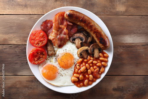 Top view of traditional full English breakfast with fried eggs bacon sausage mushrooms baked beans and tomatoes
