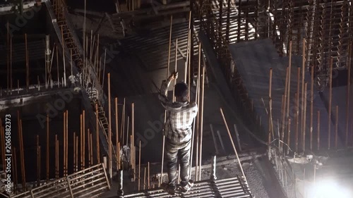 Delhi, India - 12th Mar'26: Construction worker assembling reinforced concrete structures at a building site during nighttime, illuminated by floodlights showing labor without safety