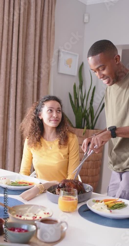 Vertical video: Couple watching man bringing roast, carving with fork knife at table for dinner
