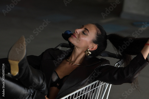 Stylish Woman in Black Leather Lying in Shopping Cart