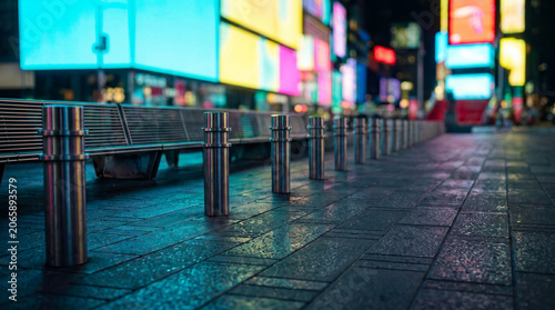 Times Square pedestrian plaza featuring a long row of bollards and benches, illuminated by colorful neon lights at night