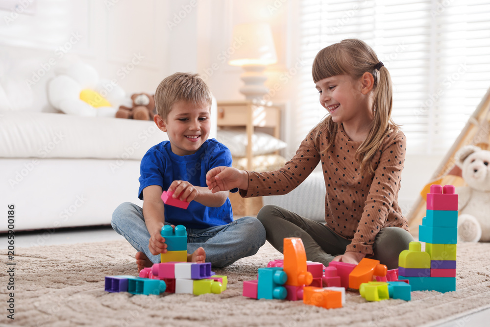 Naklejka premium Little kids playing with colorful blocks on floor at home