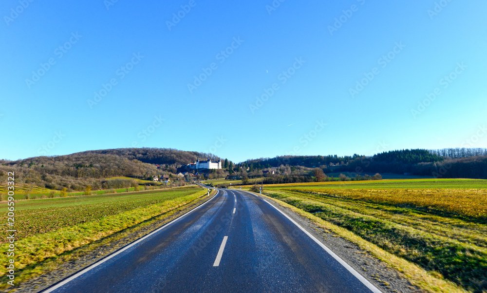 Fototapeta premium Fahrt auf einer geschwungenen Landstraße im Grabfeld mit Blick auf das Schloss Sternberg; Bayern 