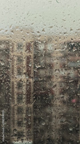 Raindrops flowing down the window glass, blurred houses and apartment buildings in the background, rainy weather and cityscape