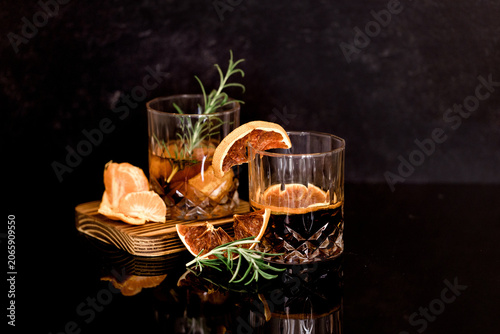 Two sophisticated dark amber bourbon cocktails garnished with dried orange and rosemary