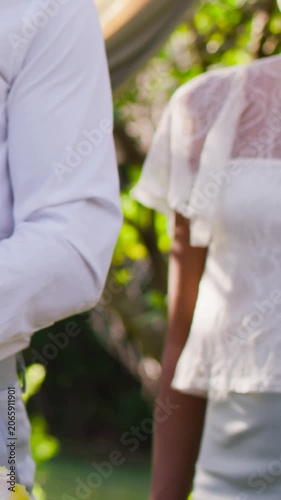Vertical video: Tilting camera showing couple in white attire readying to cut cake in yard, glass