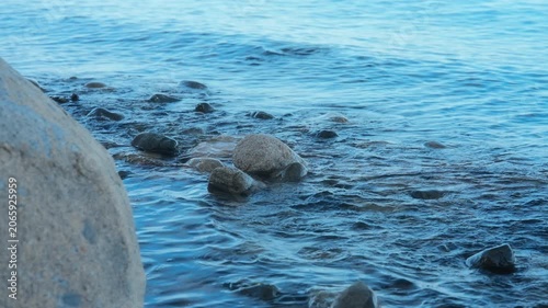 Gentle blue ocean waves washing over rocks on a peaceful stony beach