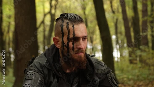 Survivalist attire, Post-apocalyptic forest, Survivalist readiness. Sitting in forest, individual with black face paint and protective gear exudes post-apocalyptic aura.