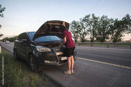 Canvas Print Woman inspecting car engine under open hood after roadside vehicle breakdown on