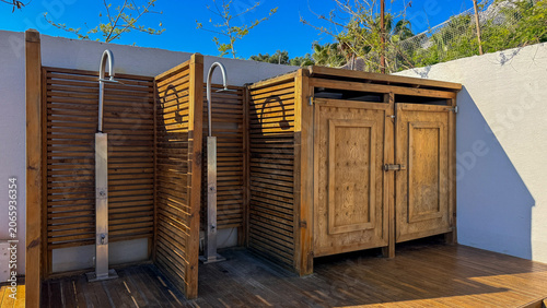 Rustic outdoor wooden showers and lockers on a sunlit deck under clear sky ideal for travel hospitality lifestyle and social media, 5 May 2026 Subitica, Serbia