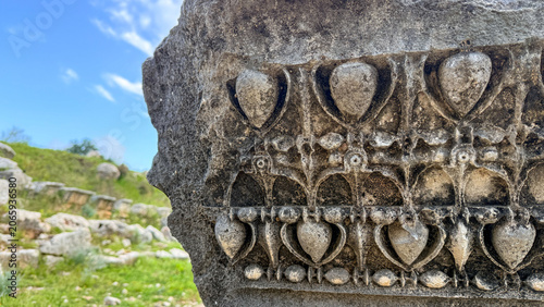 Tableau sur toile Sunlit carved stone fragment at a grassy archaeological ruin in spring evoking t