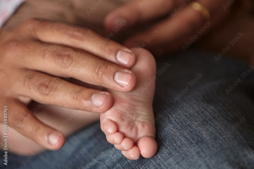 Fototapeta premium A father's strong, sun-weathered grip, wearing a leather watch strap that marks the passage of ordinary time, cradles the tiny, perfect foot of his newborn daughter with extraordinary tenderness.