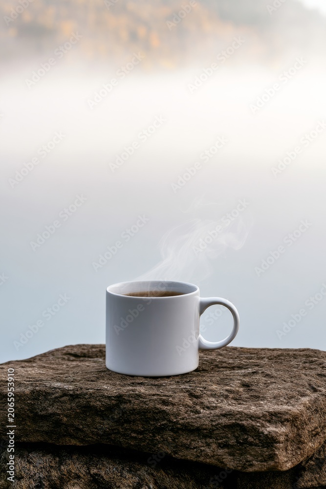 Obraz premium Steaming cup of coffee on a stone surface near water during early morning