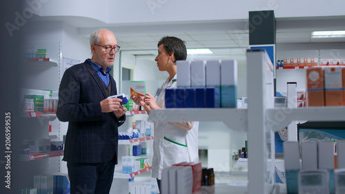 Obraz na płótnie Older man feeling unwell visiting pharmacy, looking to find pharmaceutical product to cure nauseating affliction, asking licensed healthcare employee for product suggestions