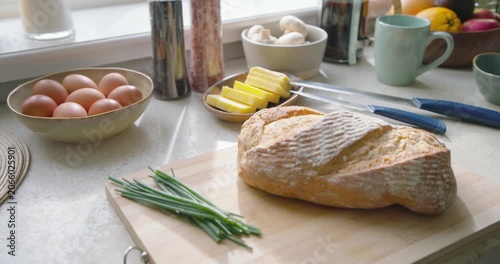 Camera is dollying by window, bringing crusty bread, butter and knives into focus for kitchen prep