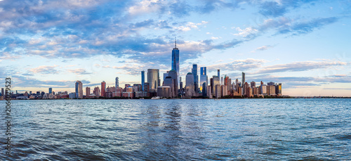 Wide-angle panoramic view of the iconic New York City skyline in the early evening, as shot across the Hudson River from the waterfront in Jersey City, New Jersey.