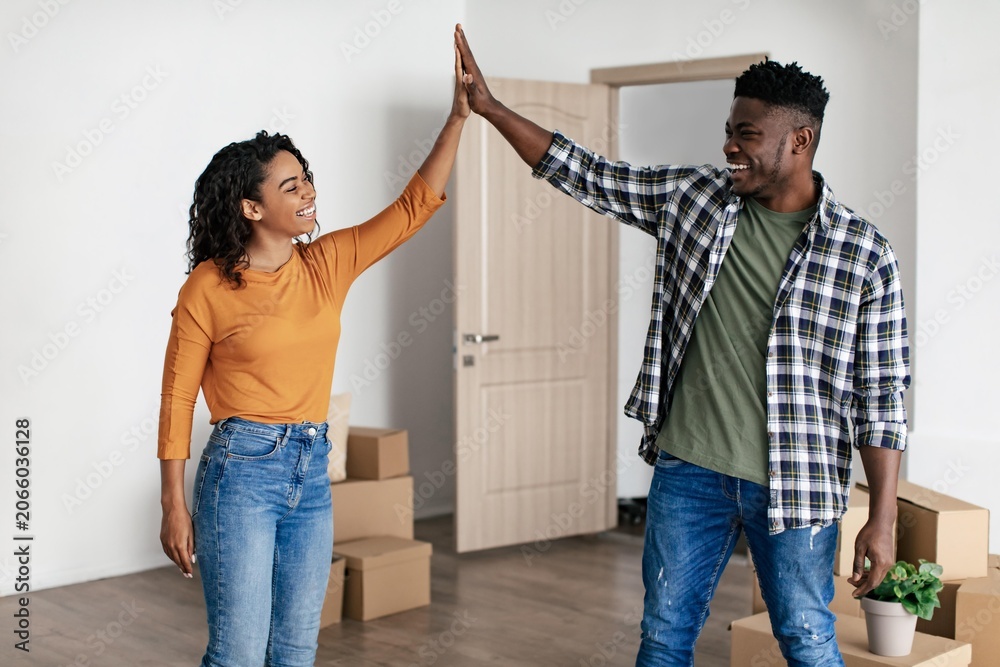 © Prostock-studio - Smiling African American Man And Woman Sharing Joyful Moment By High Fiving Each Other Inside Their New Apartment While Surrounded By Moving Boxes. Excited Young Couple Celebrating New Beginning.