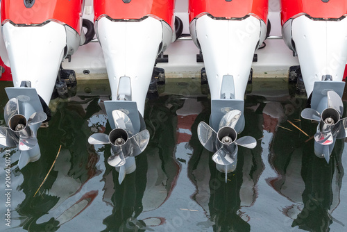 Four outboard boat motors reflected in calm marina water, creating a symmetrical pattern at a waterfront dock in New Jersey.
