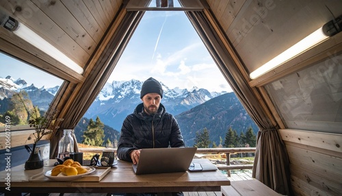 Man working on laptop in wooden cabin with mountain view