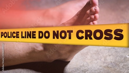 Crime scene concept with a dead body lying on the ground covered by a cloth, behind a yellow tape with the text POLICE LINE DO NOT CROSS.