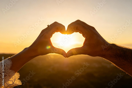 Man and woman hands framing sun in heart shape against blue sky, couple in love, romance and hopeful bright future concept