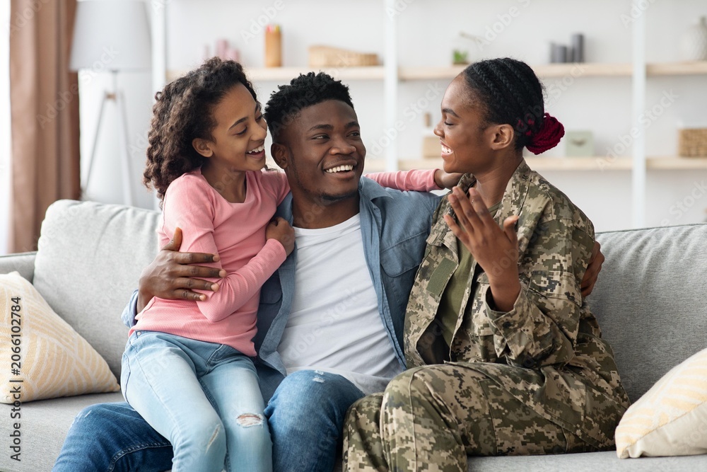 Obraz premium Happy Smiling African American Woman In Military Uniform Engaging With Two Young Daughters At Home, Creating Joyful Family Moment In Living Room, Celebrating Togetherness And Love.