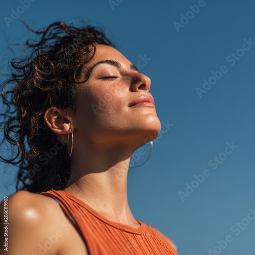 Young Woman with Curly Hair Wearing Orange Top Enjoying Sunlight in Outdoor Setting