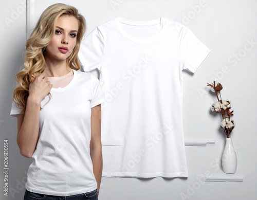 A blonde woman poses next to a white t-shirt and a vase with flowers