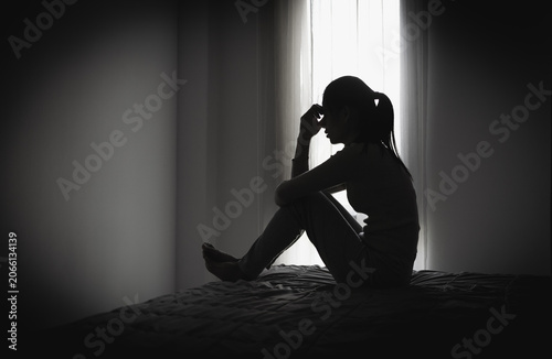 Fotografía Depressed woman sitting alone in a dark room, representing domestic violence, emotional abuse, trauma, anxiety, loneliness, fear, and mental health struggles