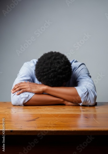 Arms and head with melanin skin lean heavily on a wooden desk, overwhelmed by office burnout, career stress, and mental health fatigue, melanin, mood, career
