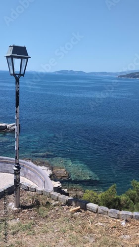 Kavala, Greece: Turquoise waters, weathered lamppost, and rocky coastline create a tranquil Aegean Sea view.