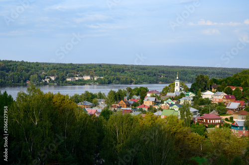 The town of Ples on the banks of the Volga River with wooden houses in a lowland covered with forest, with a church and a bell tower at sunset