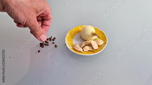 Whole onion and garlic cloves arranged on a plate with scattered peppercorns, presenting fresh cooking ingredients in a simple kitchen food preparation and seasoning scene