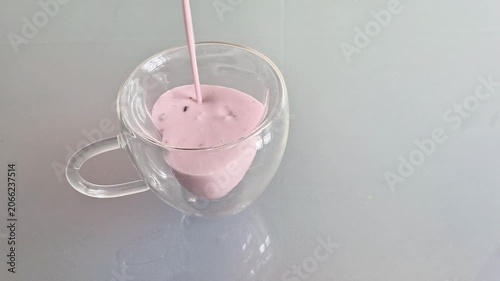 Creamy pink yogurt is poured into a clear glass cup on a reflective surface, creating a smooth swirl. Minimal food preparation scene showcasing freshness, texture, and simple serving