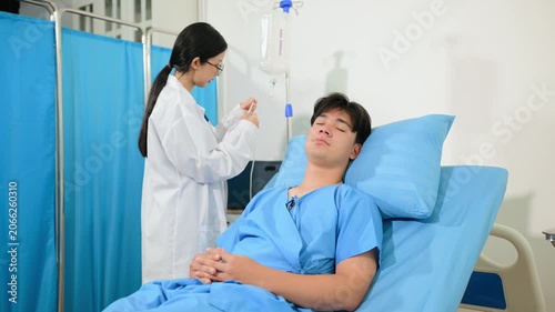 Female doctor adjusting an IV drip for a young male patient resting in a hospital bed. Professional healthcare and medical treatment